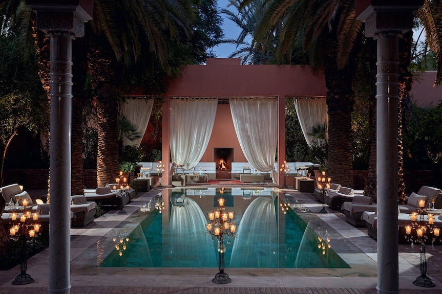 Luxury outdoor pool area at Royal Mansour Marrakech with elegant seating, palm trees, and illuminated candelabras at dusk