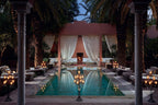 Luxury outdoor pool area at Royal Mansour Marrakech with elegant seating, palm trees, and illuminated candelabras at dusk