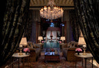 Luxury Moroccan-style riad living room with dark embroidered curtains, plush sofas, crystal chandelier, and pool view at Royal Mansour Marrakech