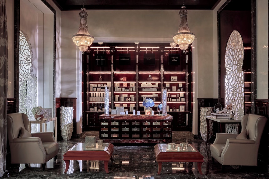 Luxury spa reception area at Royal Mansour Marrakech with dark wood shelves, crystal chandeliers, marble floor, and beige armchairs