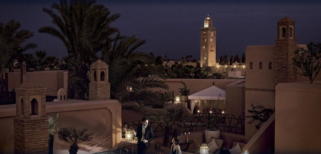 Royal Mansour Marrakech terracotta-colored buildings with traditional Moroccan architecture and palm trees at dusk with illuminated minaret in background