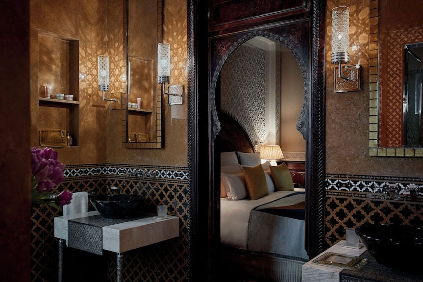 Royal Mansour Marrakech bathroom with intricate Moroccan tilework, warm brown and black tones, ornate wall sconces, and a glimpse of a luxurious bedroom
