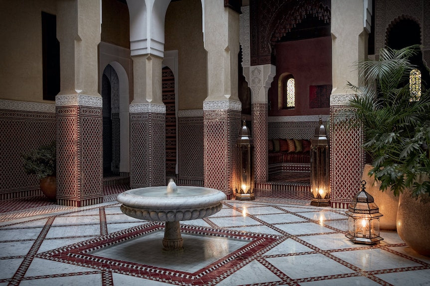 Royal Mansour Marrakech courtyard featuring intricate Moroccan tilework, arched columns, a central stone fountain, and traditional lanterns