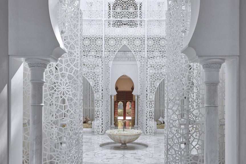 Royal Mansour Marrakech interior with white intricate Moroccan latticework, marble columns, arches, and central stone fountain