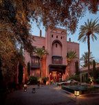 Royal Mansour Marrakech luxurious Moroccan-style building with pink stucco walls, palm trees, lanterns, and courtyard fountain at dusk