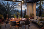 Outdoor dining area at Royal Mansour Marrakech featuring a round wooden table set with glassware and surrounded by wicker chairs and cushioned sofa under hanging lanterns
