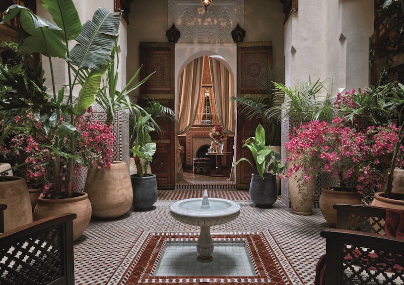 Royal Mansour Marrakech courtyard with traditional Moroccan tile floor, central stone fountain, lush potted plants, and ornate carved wooden doors