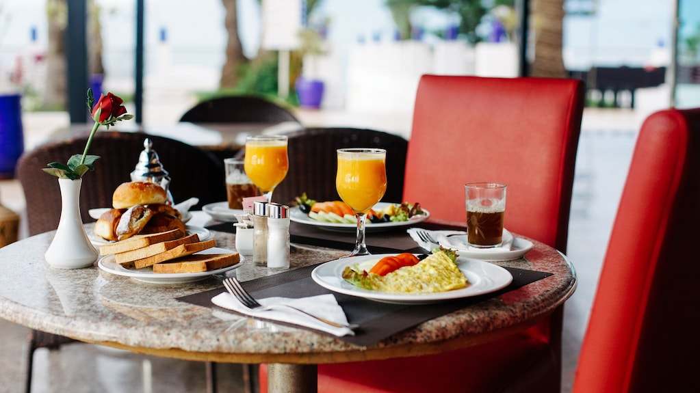 Royal Mirage Agadir restaurant table with breakfast plates, bread, orange juice, coffee, and red upholstered chairs