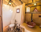 Bathroom interior at Sahara dunes Luxury Camp featuring beige fabric walls, decorative ceramic sink, toilet, and woven basket