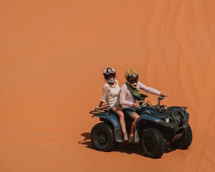 Sahara dunes Luxury Camp adventure with two people riding a blue all-terrain vehicle on vast orange sand dunes under clear skies