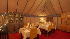 Sahara dunes Luxury Camp dining tent with tan fabric walls, wooden cabinets, tables with white cloths, candles, and cushioned chairs