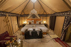 Sahara dunes Luxury Camp spacious tent bedroom with tan fabric walls, large bed, patterned cushions, and decorative rugs