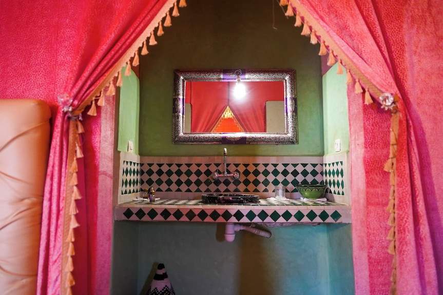 Sahara Garden Luxury Camp bathroom interior featuring a green wall, geometric tiled sink, decorative mirror, and pink tassel curtains