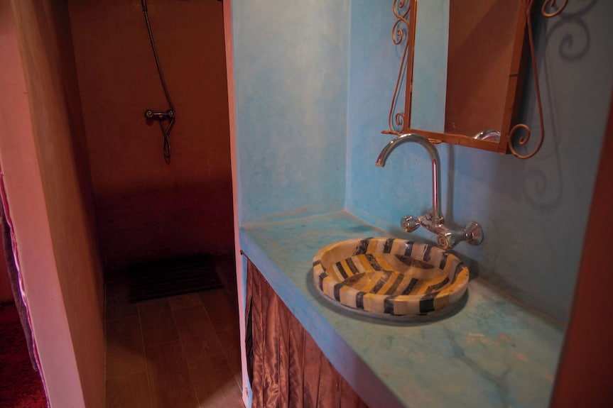 Bathroom sink with colorful striped basin and chrome faucet set in light blue Moroccan style countertop at Sahara Garden Luxury Camp