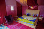 Sahara Garden Luxury Camp bedroom featuring a large bed with colorful pillows, yellow quilt, purple armchair, and red carpet