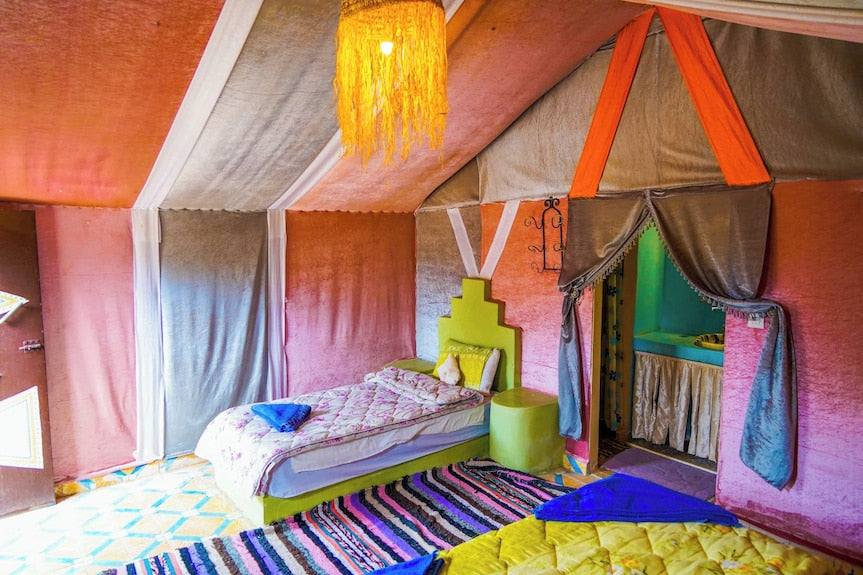 Sahara Garden Luxury Camp interior featuring colorful tent walls, patterned rug, green bed with quilt, and decorative hanging light