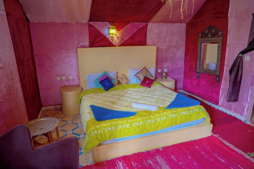 Sahara Garden Luxury Camp bedroom with colorful pink and red fabric walls, a beige bed with yellow and blue bedding, and patterned pillows