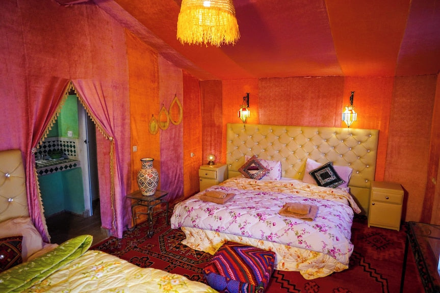 Sahara Garden Luxury Camp interior with warm orange walls, floral bedding, colorful cushions, and traditional Moroccan decor