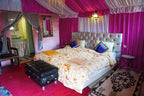 Luxury tent bedroom at Sahara Garden Luxury Camp with vibrant pink draped walls, tufted bed, floral quilt, and decorative pillows