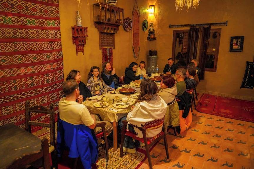Sahara Garden Luxury Camp Moroccan dining room with traditional carpets, warm lighting, and guests enjoying a meal together
