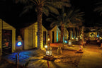 Sahara Garden Luxury Camp at night featuring illuminated beige luxury tents, palm trees, and decorative lanterns lining a sandy path
