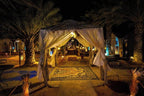 Sahara Garden Luxury Camp nighttime entrance with illuminated white fabric canopy, patterned carpets, and palm trees