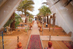 Sahara Garden Luxury Camp outdoor pathway with traditional Moroccan rugs, palm trees, terracotta lanterns, and desert sand ground