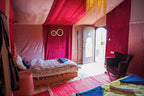 Sahara Garden Luxury Camp room with red and pink fabric walls and ceiling, two beds with colorful blankets, a black armchair, and a decorated door