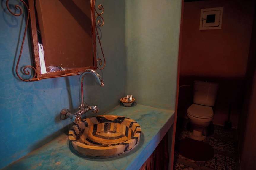 Bathroom interior at Sahara Garden Luxury Camp featuring a striped stone sink, curved silver faucet, and turquoise plaster counter