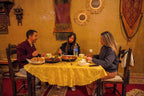 Dining scene inside Sahara Garden Luxury Camp with three people eating traditional Moroccan meal at round table with yellow tablecloth