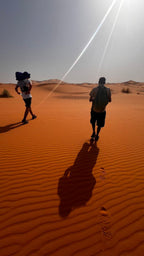 Sahara Trek Camp featuring two people walking on orange sand dunes under bright sunlight with clear blue sky