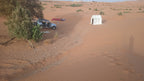 Sahara Trek Camp showing a white canvas tent and silver 4x4 vehicle parked near sparse greenery in sandy desert dunes under clear sky