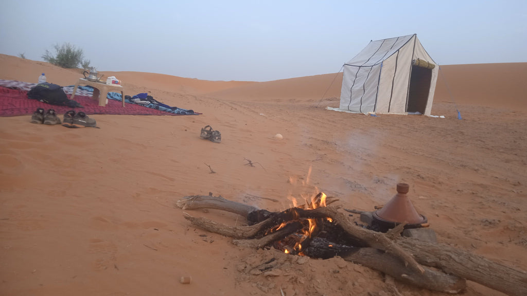 Sahara Trek Camp with white canvas tent, campfire burning on desert sand under clear sky