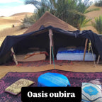Sahara Wild Camp brown canvas tent with two single beds, cushions, blue table, and traditional rugs in desert oasis