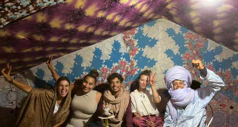 Sahara Wild Camp group of five people in colorful traditional tent with patterned fabric walls and ceiling smiling and posing