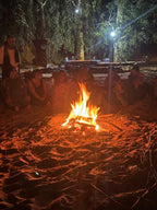 Sahara Wild Camp at night with a bright campfire surrounded by people sitting on sand under trees