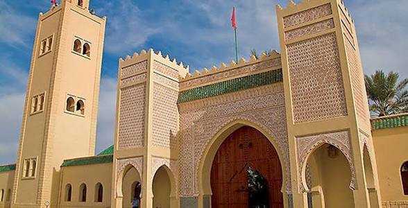 Historic Moroccan sandstone gate with intricate carvings and arched wooden doors under a blue sky in shared 3 days 2 nights tour