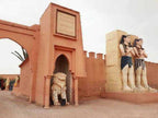 Entrance gate with terracotta-colored walls and statues, featuring a lion sculpture and two Egyptian-style figures, representing shared 3 days 2 nights desert tour.