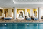 Indoor swimming pool with blue tiled water, beige patterned floor, and arched openings featuring lounge beds at Sofitel Marrakech Palais Imperial & Spa