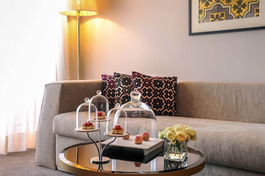 Sofitel Marrakech Palais Imperial & Spa beige fabric sofa with patterned cushions next to a glass coffee table with desserts under glass cloches and white roses