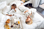 Couple in white bathrobes enjoying breakfast with pastries, tea, and orange juice on a bed at Sofitel Marrakech Palais Imperial & Spa