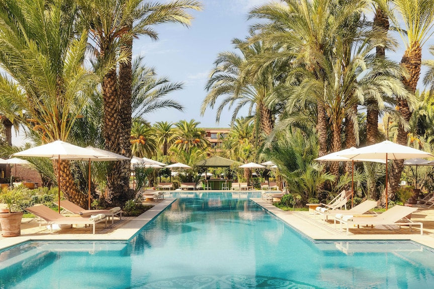 Sofitel Marrakech Palais Imperial & Spa outdoor pool surrounded by palm trees, sun loungers, and white umbrellas under clear sky