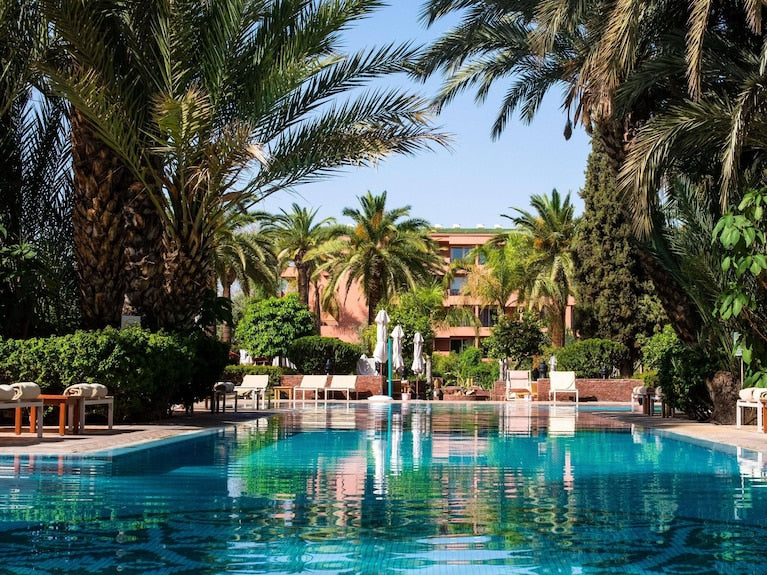 Sofitel Marrakech Palais Imperial & Spa outdoor pool surrounded by palm trees and lounge chairs with clear blue sky