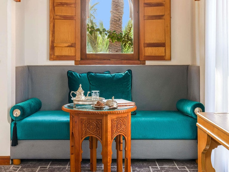 Sofitel Marrakech Palais Imperial & Spa seating area with turquoise cushions and an intricately carved wooden table under a wooden window