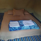 Standard Camp Merzouga Oasis simple beige bed inside a desert tent with pillows and blue patterned blanket topped with folded white towels