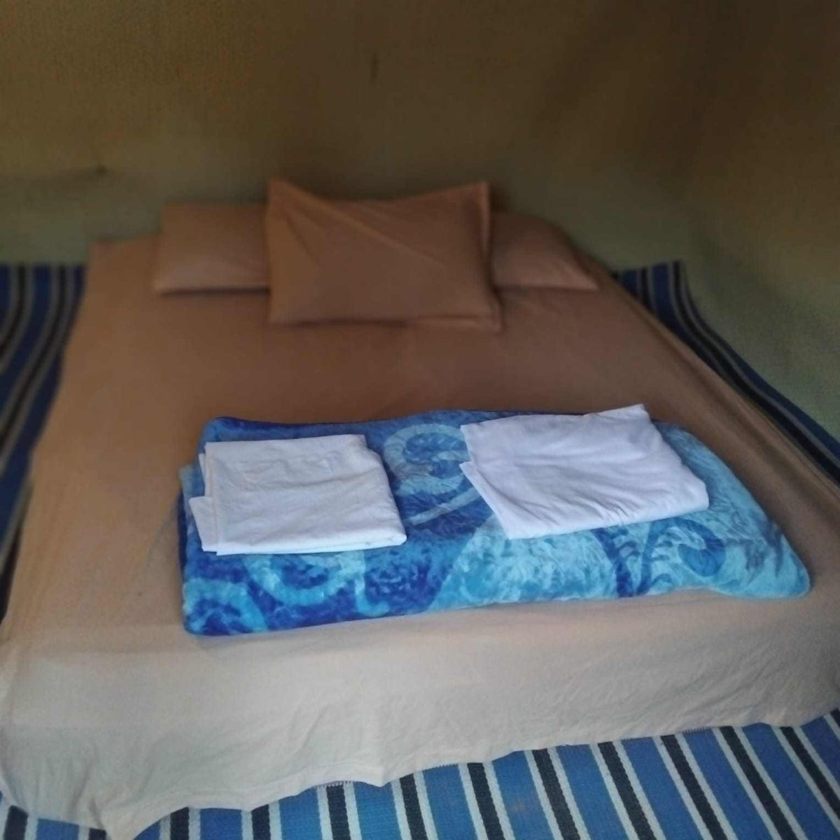 Standard Camp Merzouga Oasis simple beige bed inside a desert tent with pillows and blue patterned blanket topped with folded white towels
