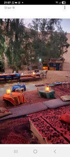 Standard Camp Merzouga Oasis outdoor seating with colorful patterned rugs, cushions, low tables, and lanterns in a desert setting