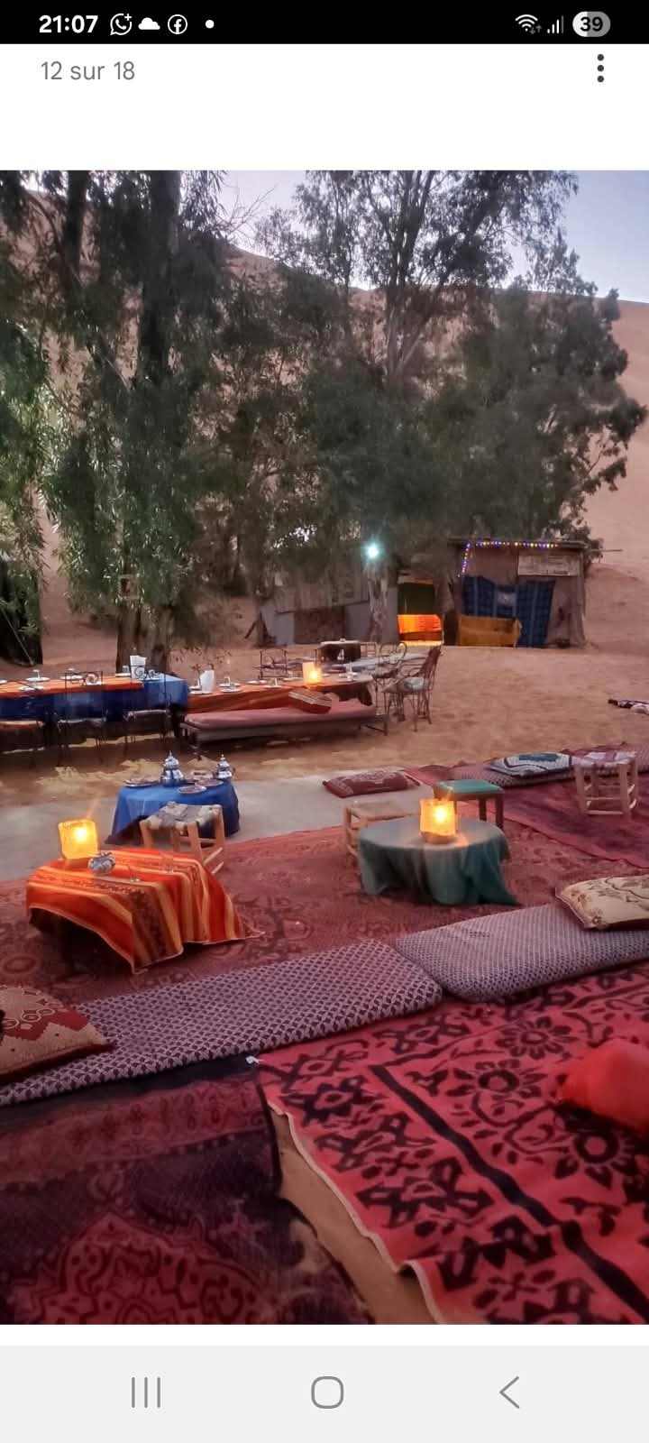 Standard Camp Merzouga Oasis outdoor seating with colorful patterned rugs, cushions, low tables, and lanterns in a desert setting