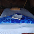 Standard Camp Merzouga Oasis tent bed with white sheets, beige pillow, and blue patterned blanket for desert comfort