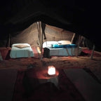 Standard Camp Merzouga Oasis showing traditional desert tent with two single beds and a glowing lantern on a carpeted floor at night